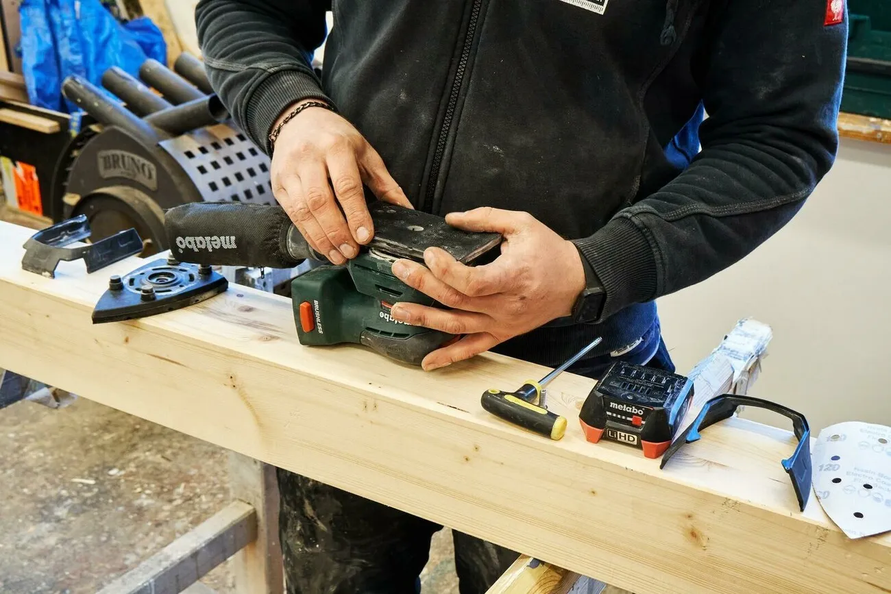 Handwerker tauscht die dreieckige Schleifplatte durch eine quadratische aus.